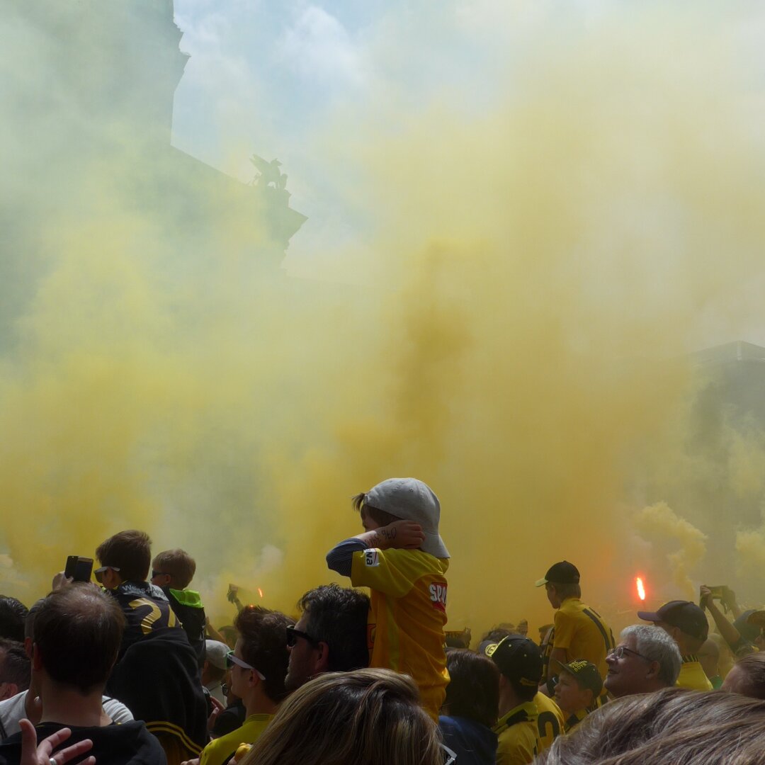 an image from my Pixelfed (because, fuck instagram), in a crowd in yellow smoke, one kid sits on his fathers shoulder and holds his ears shut