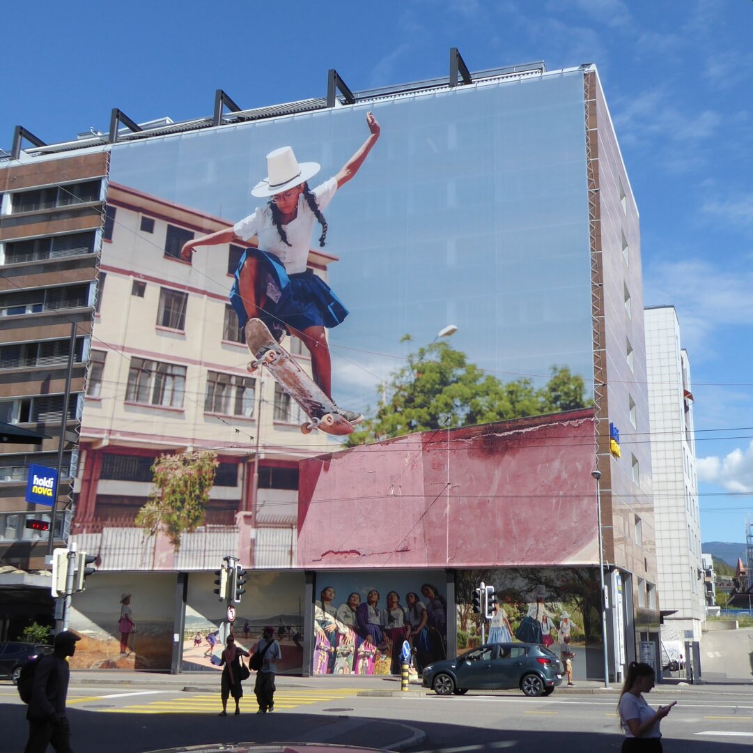 an image from my Pixelfed (because, fuck instagram), a very large photo on a wall shows a skateboarding Peruvian woman in traditional attire