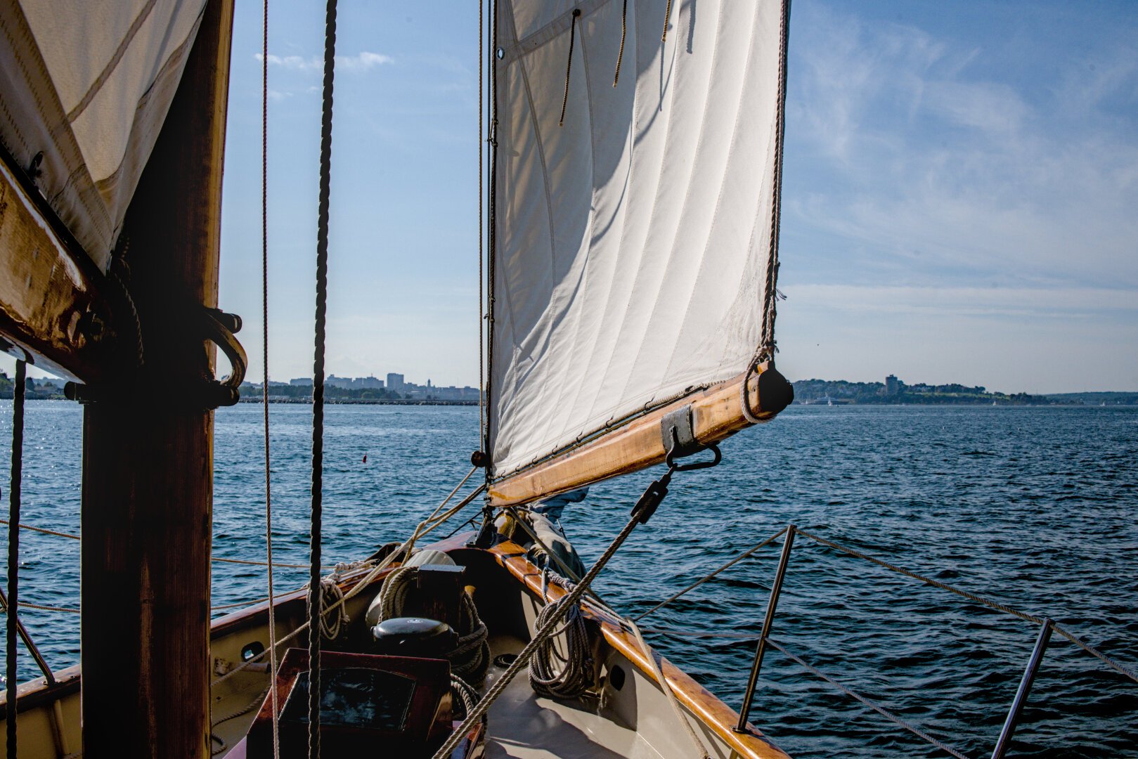 Image of the bottom of a staysail at the bow of a schooner with horizon in the background, blue sky, and water