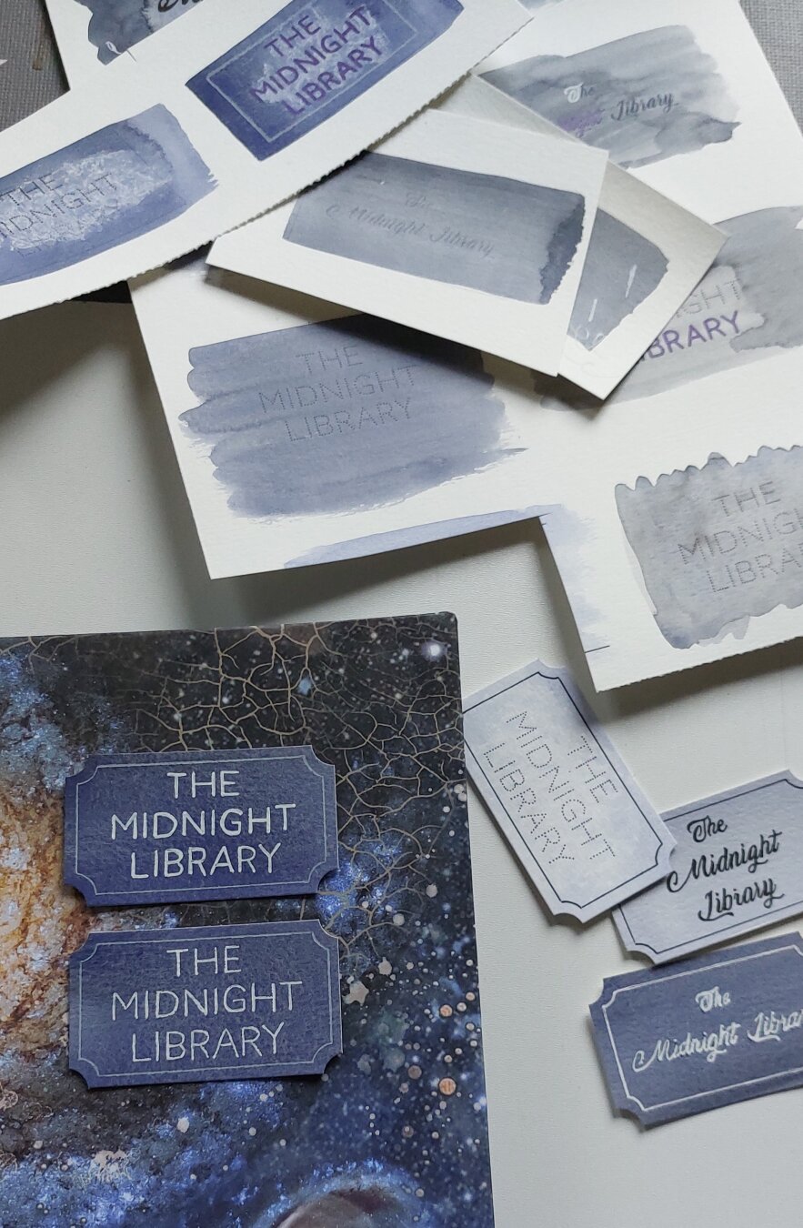 Part of book cover in dark blue space pattern with various labels placed on and around the book reading 'the midnight library '