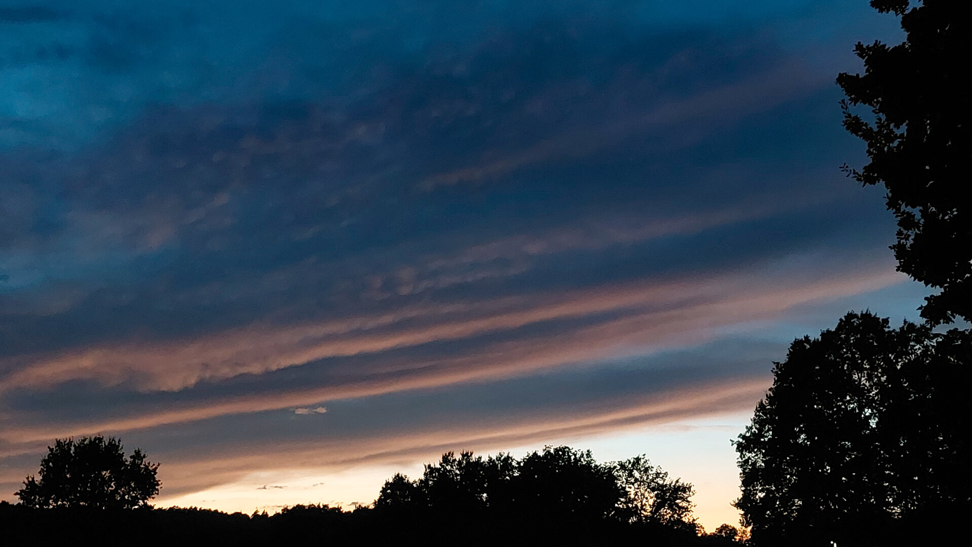 Horizontal band of dark clouds with pink bottom lining ofer black shadow forest