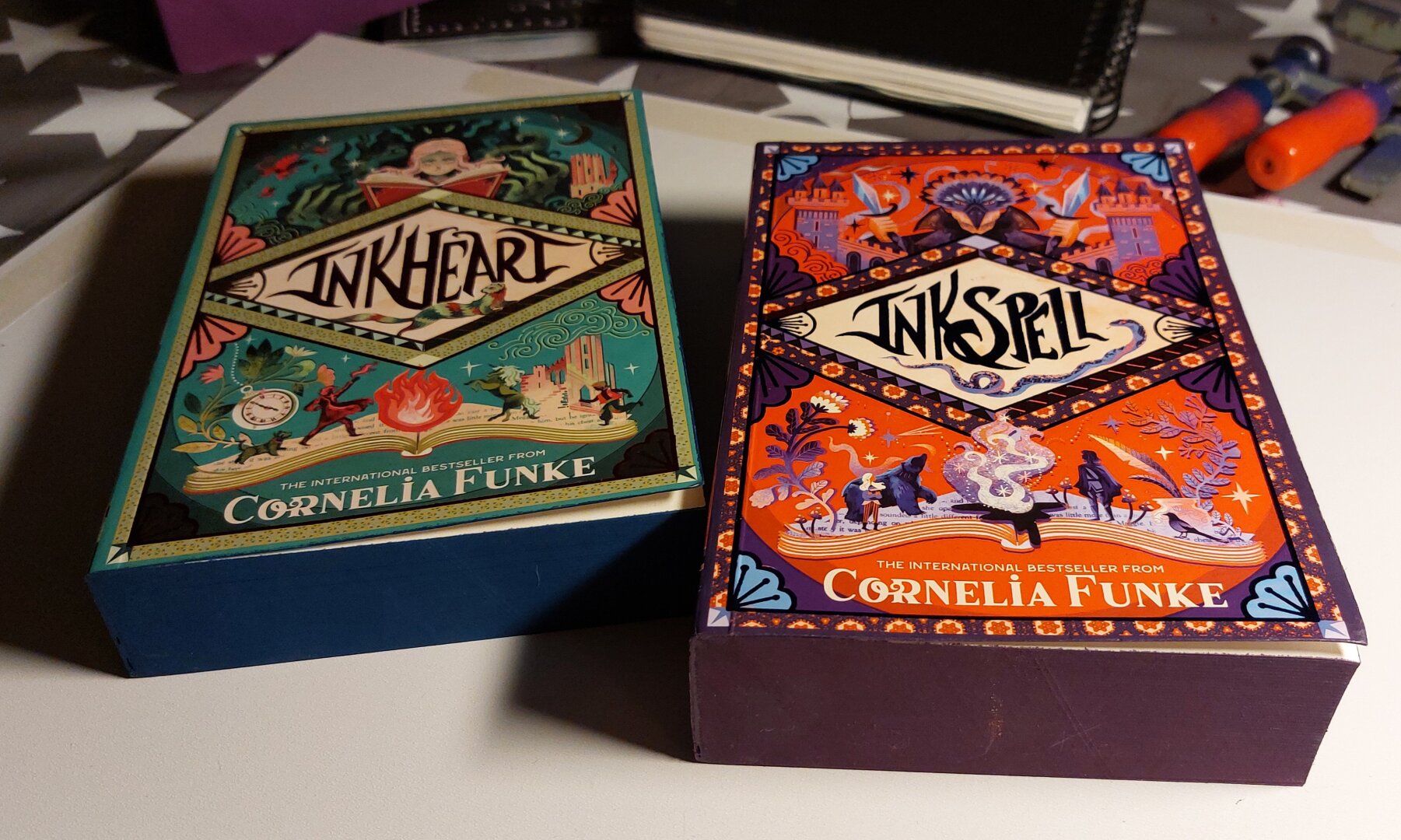 Two books from Cornelia Funke, Inkheart and Inkspell, with colorful covers and painted book edges lying on a craft table