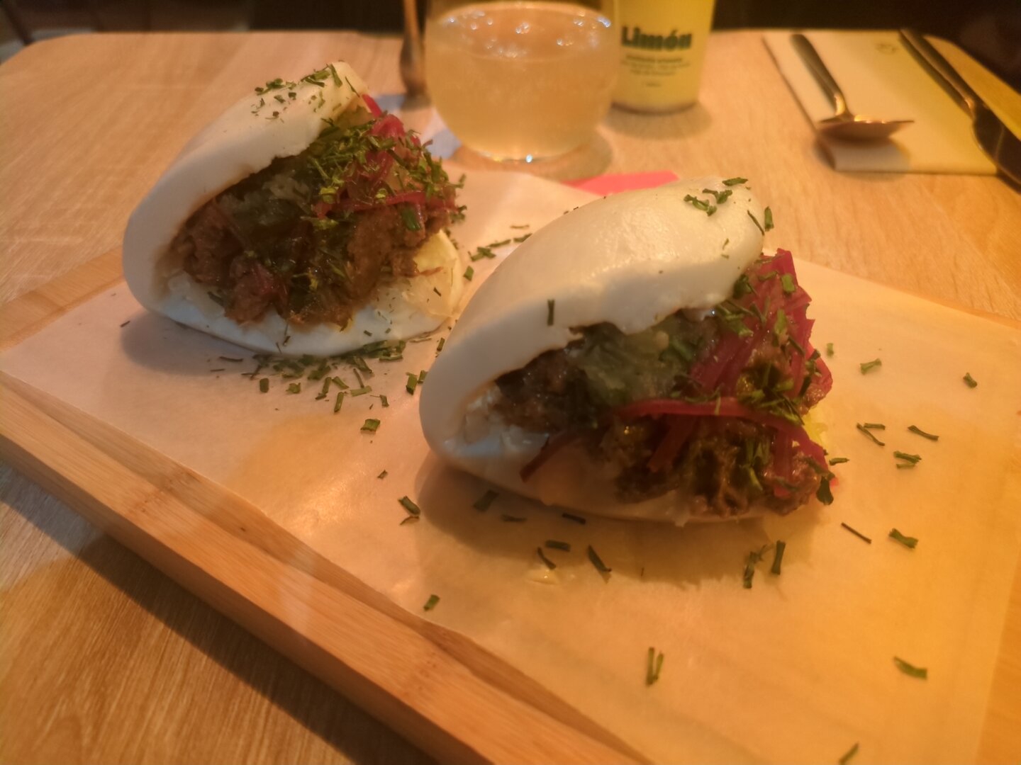 Photograph of two boas arranged like the previous dishes. The baos contain pea based pulled pork, pickled cucumber, beetroot and further ingredients.