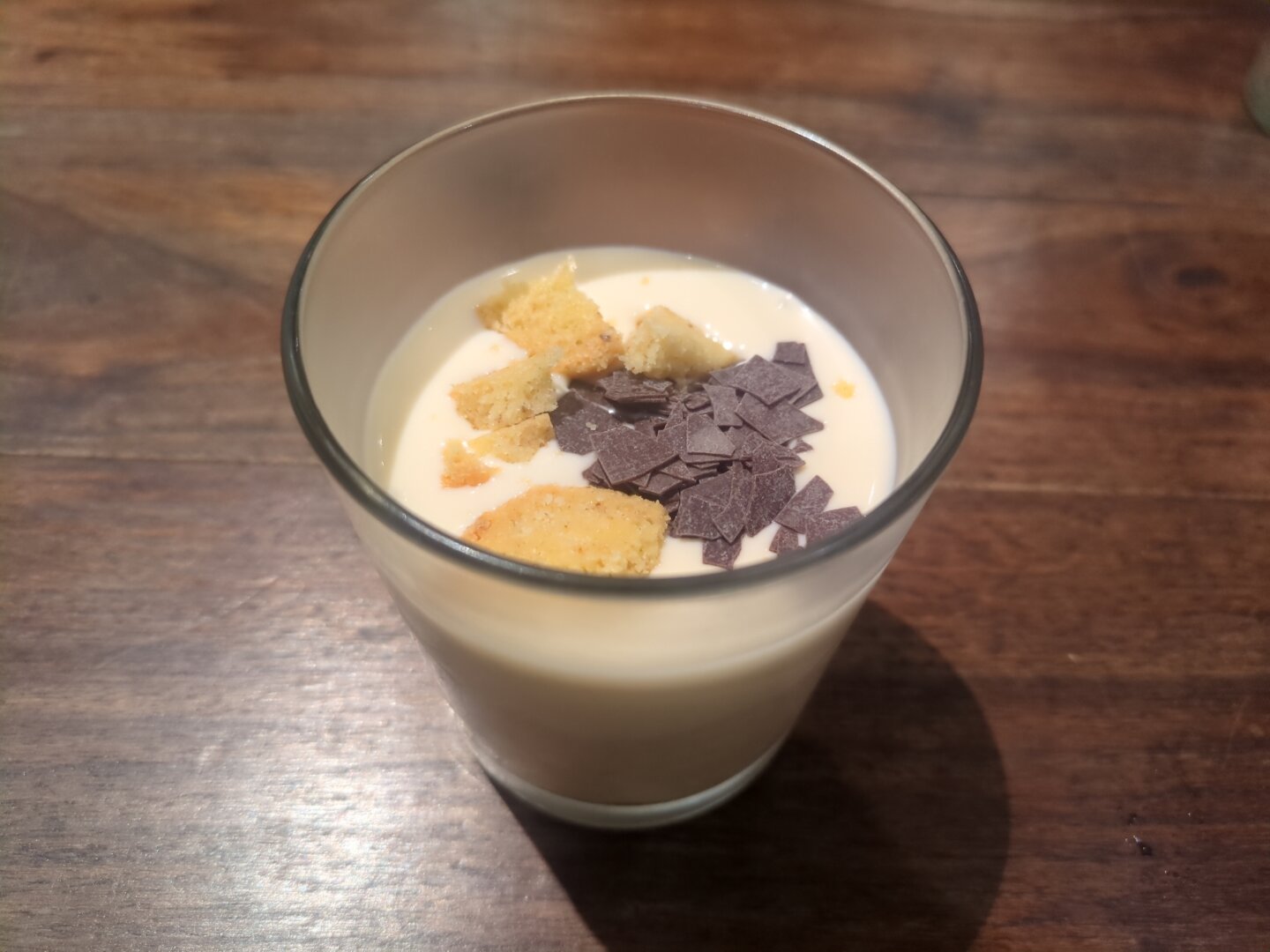 Photograph of a small glass containing a bright cream topped with dark chocolate chips and dries apple pieces.