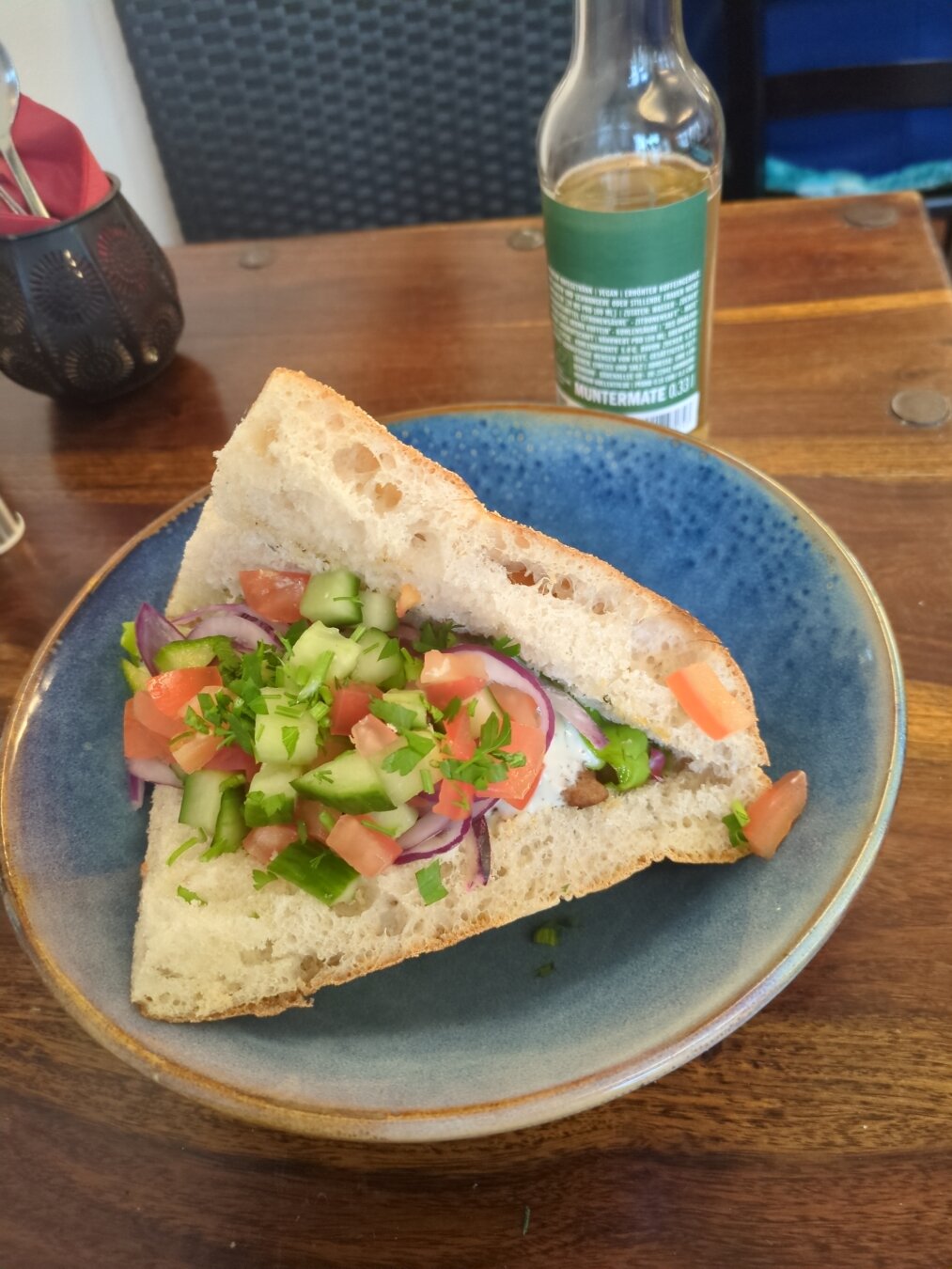 Photograph of a döner on a blue plate, located on a wooden table.