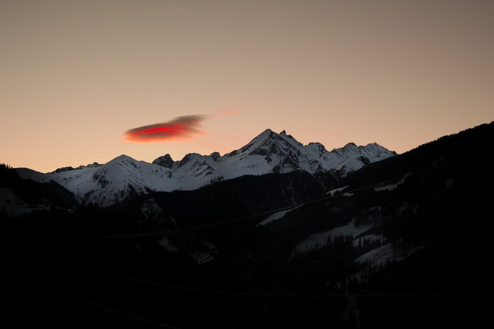 morning mood in the mountains. the sun is just rising behind the mountains and illuminates a single cloud blood red.