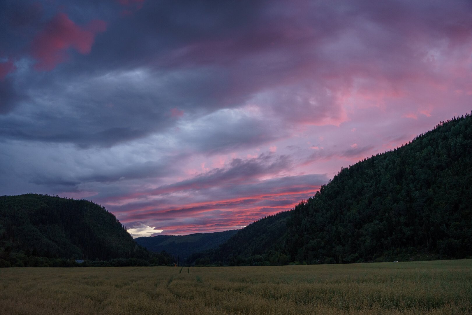 A sunset lighting up clouds with purple and magenta colors. Flanked by tree covered cliff sides.