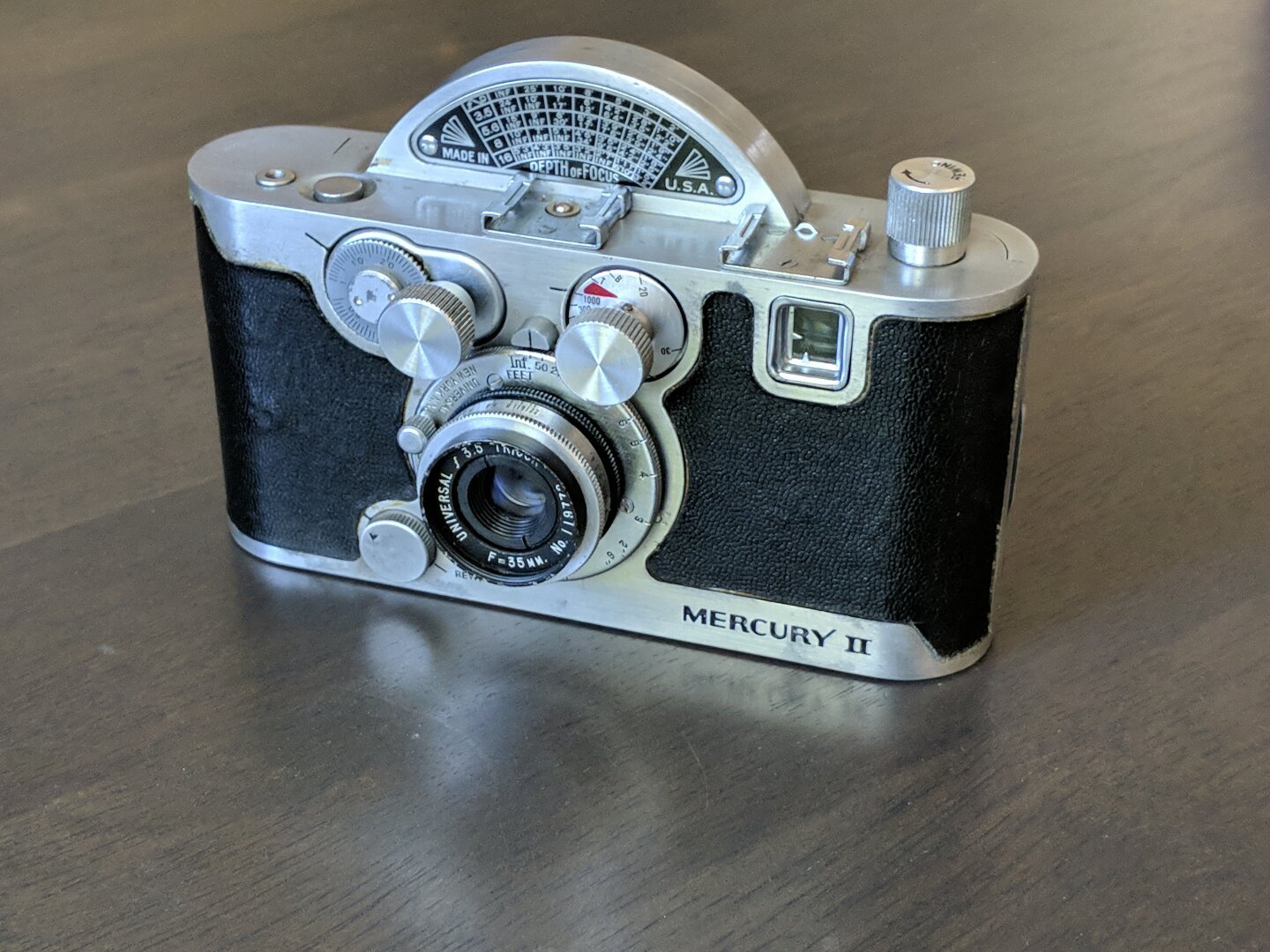 A small alloy body camera. A large disc protrudes from the top, this houses the rotary shutter as well as display a convenient depth of field chart.

The from has a number of knobs protruding for shutter cocking and film advance, as well as shutter speed.