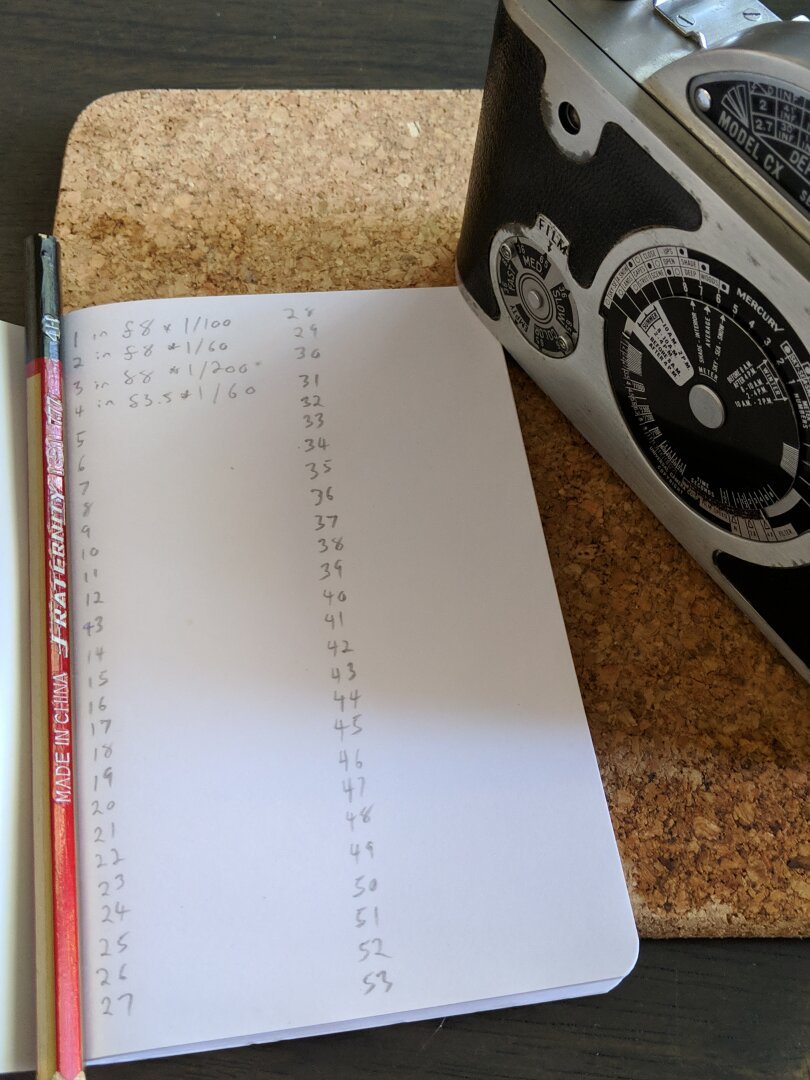 A note book lays open on a cork mat beside a small camera.

The notebook has entries numbered 1 through 53, only the first 4 have data.

It is a record of settings for each frame shot.