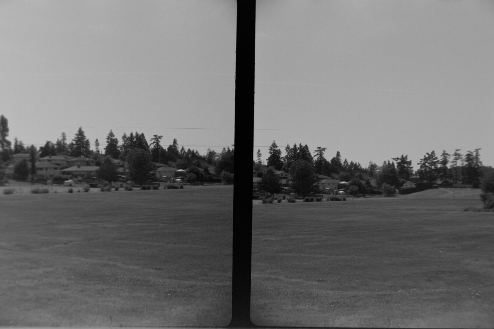 Two portrait frames. A view of some houses and trees across a large grass field.