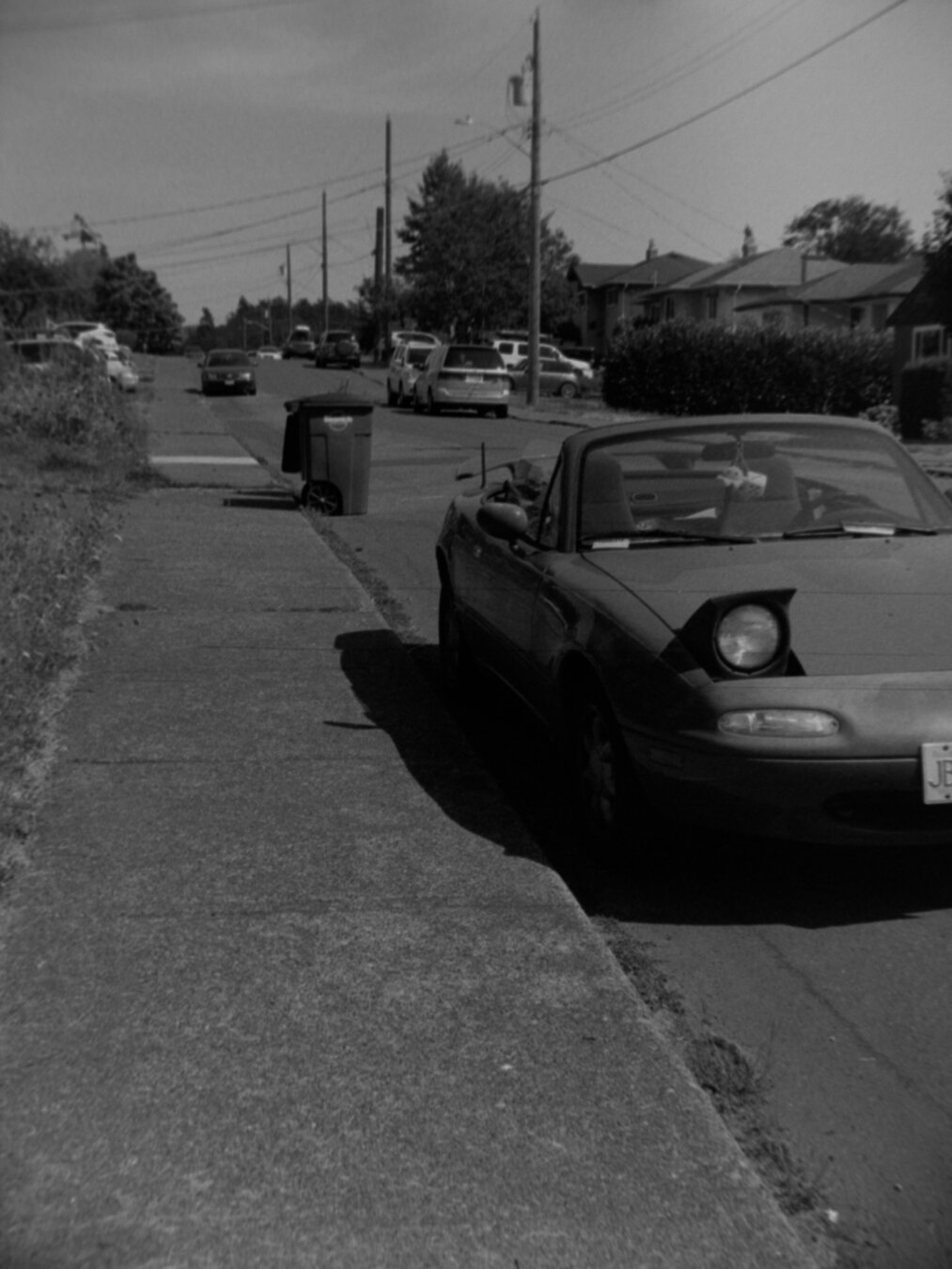 A small convertible with the top down, parked on the side of a quite street.