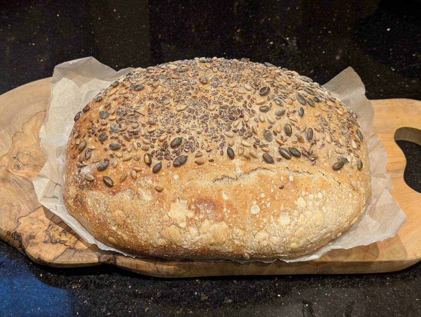 A pretty reasonable-looking oval loaf of sourdough cooling off on a wooden block. It has seeds on top.