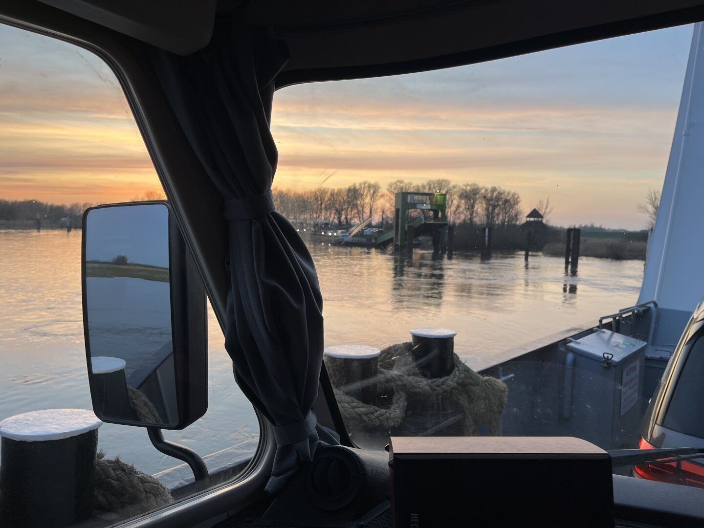 Blick durch die Frontscheibe Hymer B574 auf der Elbefähre Richtung Anleger Wischhafen. Sonnenuntergang und kahle Bäume im Hintergrund