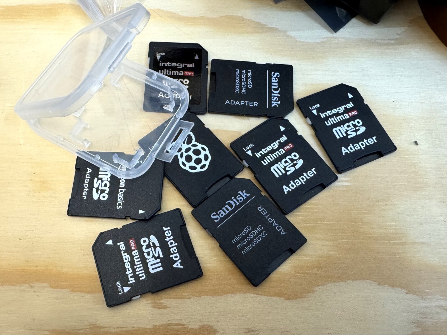 A number of SD cards - adapters for microSD cards - scattered on a wooden tabletop.