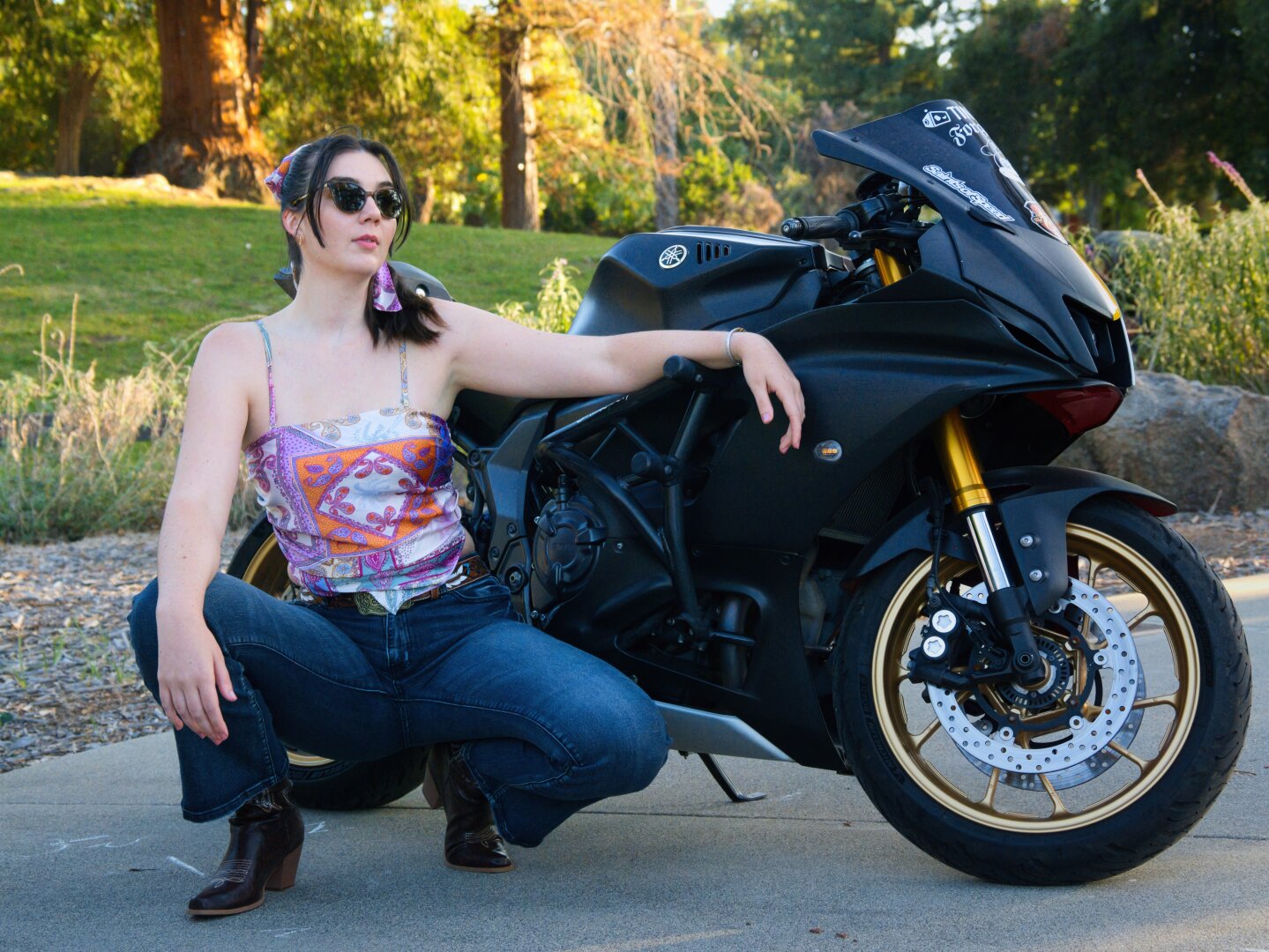 A brunette woman squatting next to a motorcycle