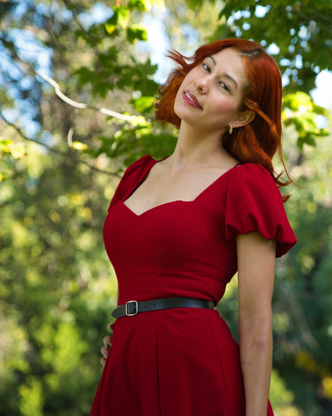 A woman in a red dress with branches full of green leaves in the background.