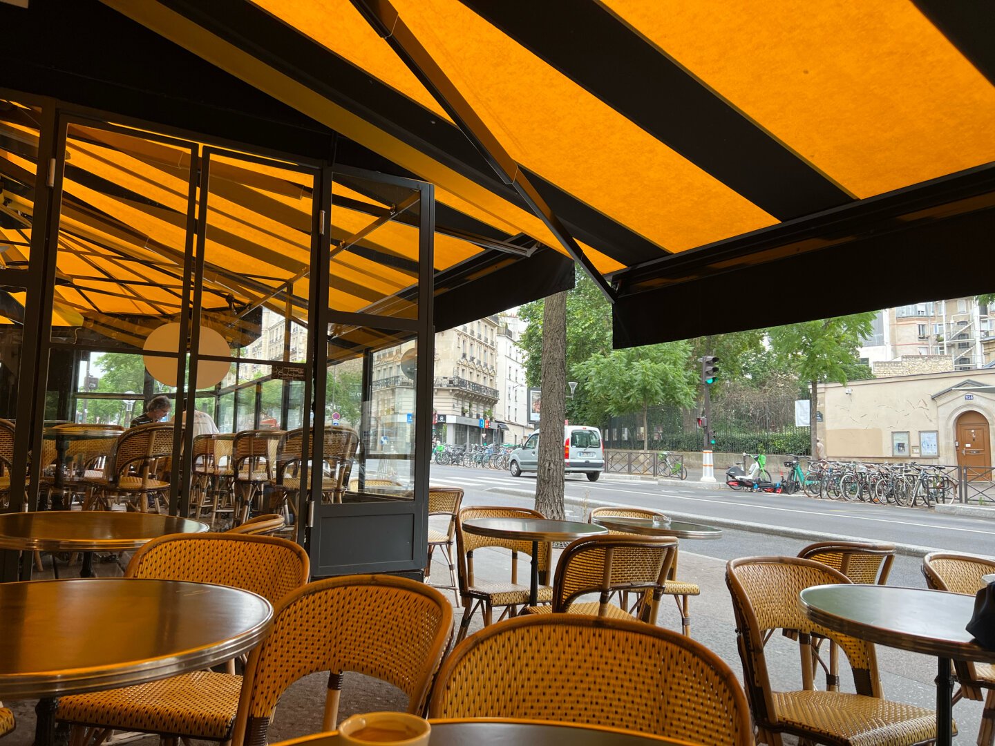 In a coffee patio, under a yellow canopy. Grey street. It's raining.