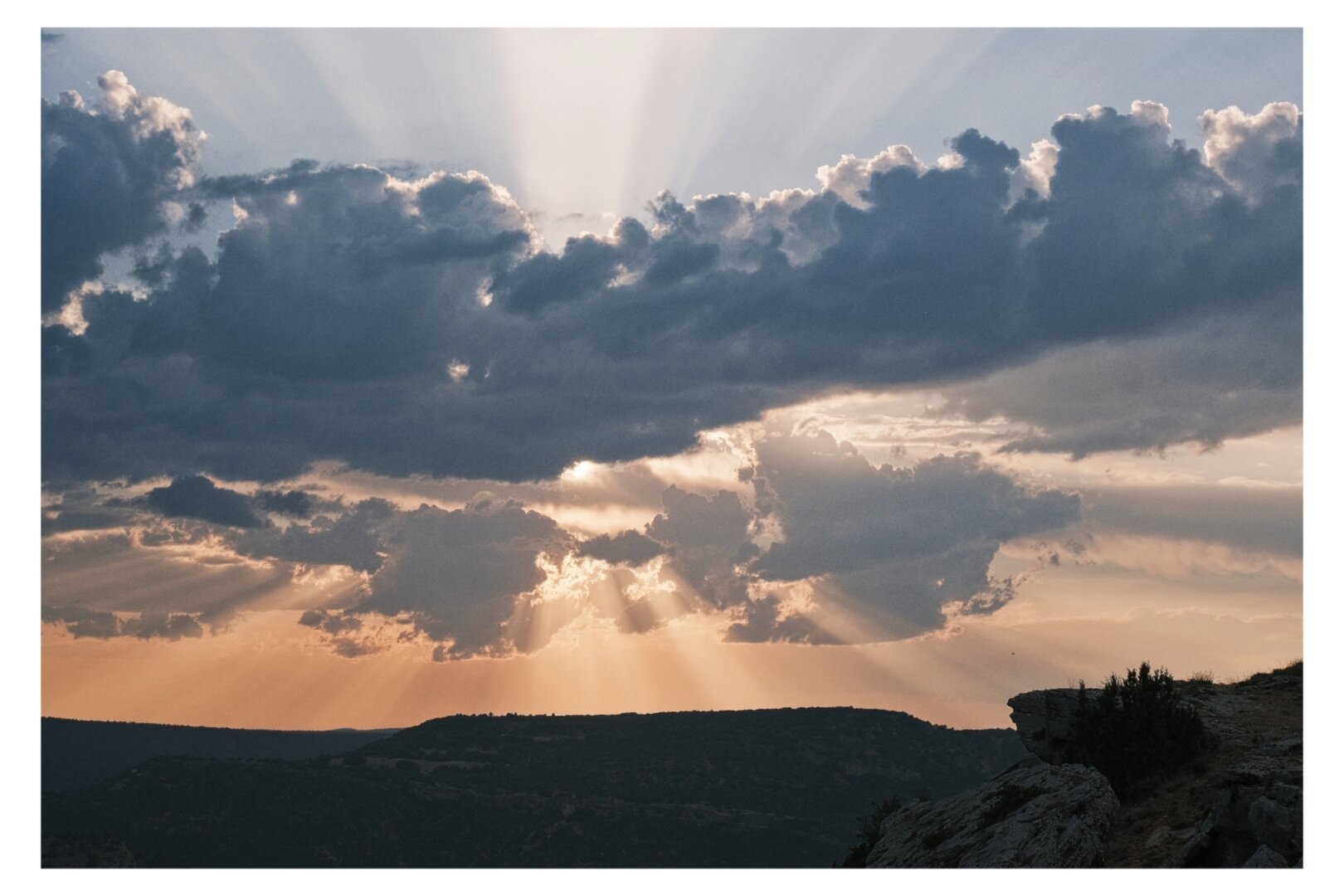 A shot of the sky looking west, with some clouds hiding the sun. Crepuscular rays are seen through the clouds.