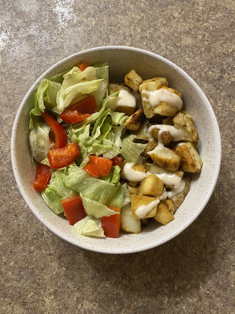 A bowl with lettuce and red peppers on the left and potatoes and tofu on the right topped with garlic mayo