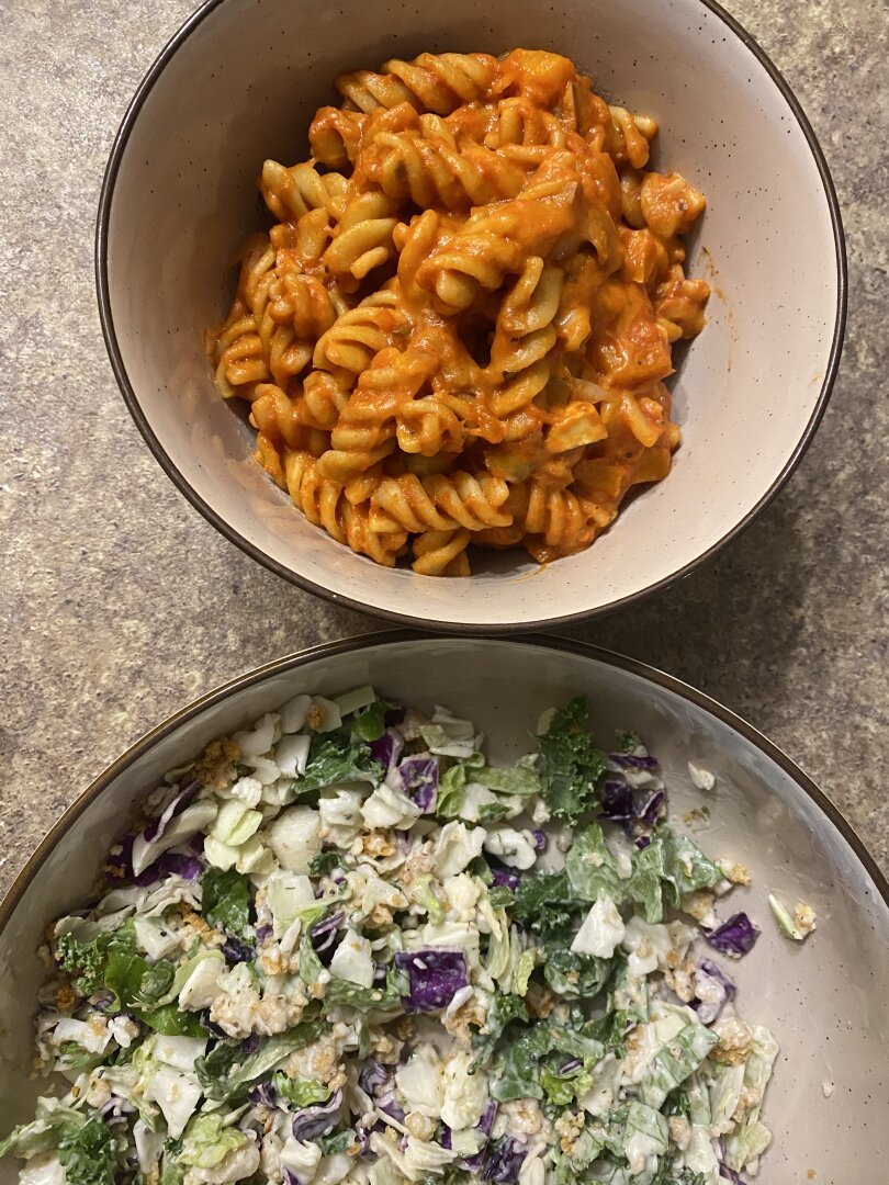 A pasta bowl with fusili in a red tomato sauce. Next to it is a big plate/bowl with a salad