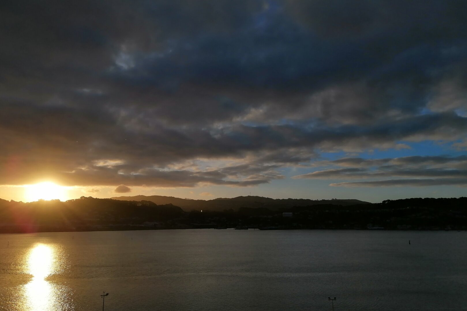 Sunset on Evans Bay with the sun between clouds and the Wellington hills