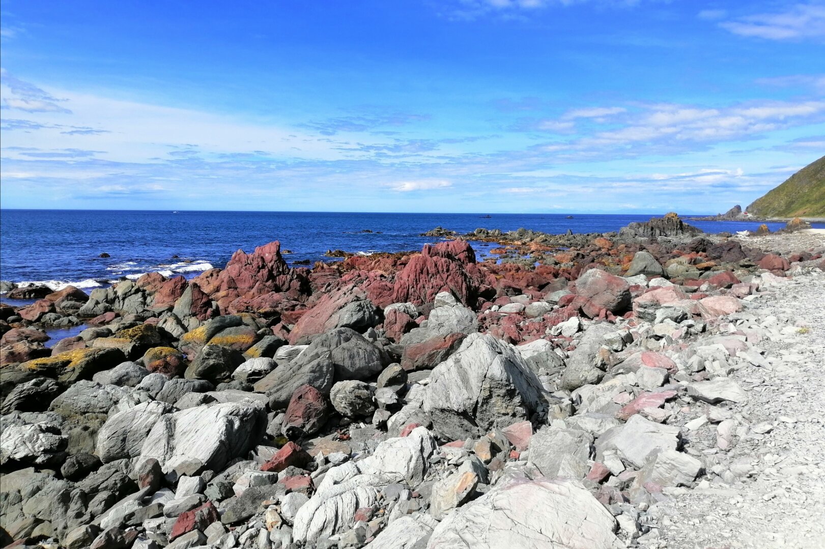 Red Rocks amongst grey and green ones on the water's edge