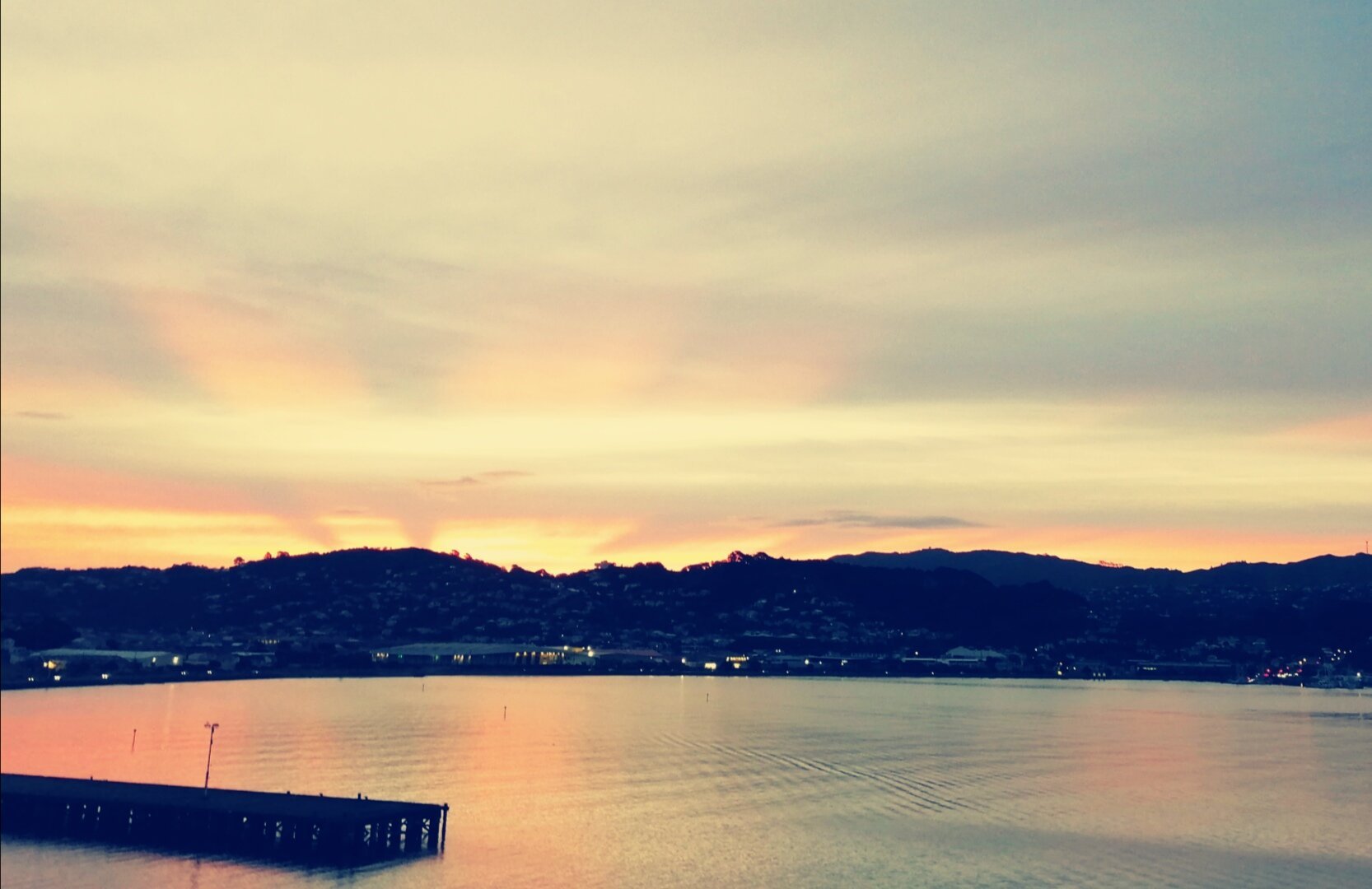 Sunset with 2 distinct rays going up into the clouds with Evans Bay in front