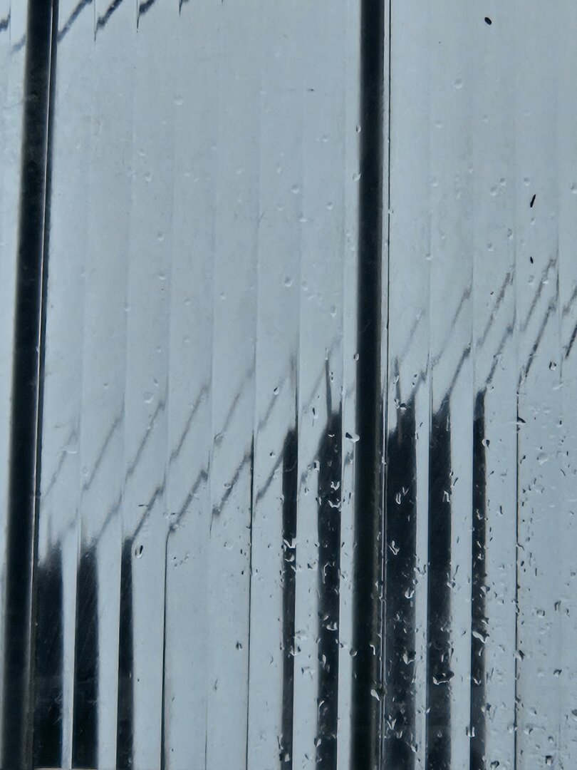 A glass window with vertical streaks and raindrops, creating a blurred and distorted effect of the external landscape.