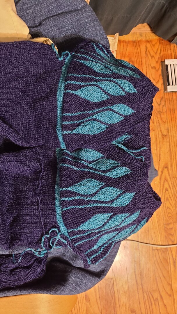 The yoke and upper body of a partially finished cardigan. The main colour is navy and the yoke has dramatic teal leaves in short row colour work.