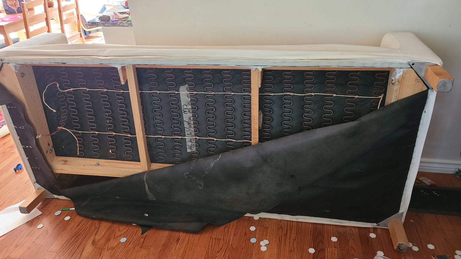 A view from the bottom of the couch reveals a spring that is no longer attached