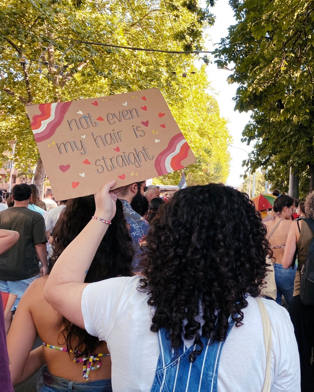 Una ragazza riccia con un cartello “not even my hair is straight”