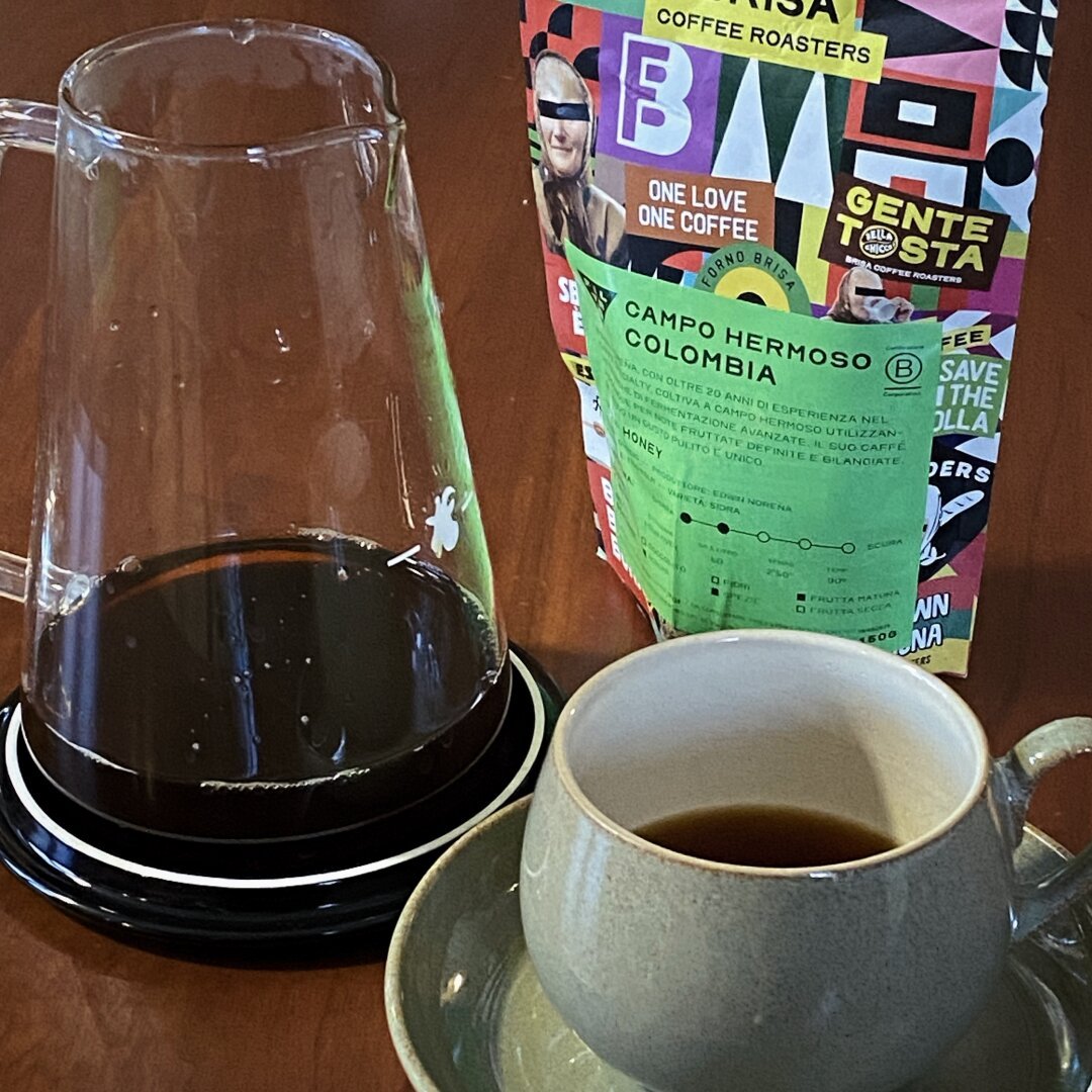 Cup of drip coffee on a table with the coffee bag behind, the label says “campo Hermo Colombia”