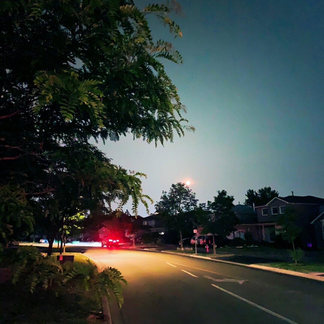 Strawberry Full Moon, there is a car parked by the side of a suburban road, the brake lights a full on red.