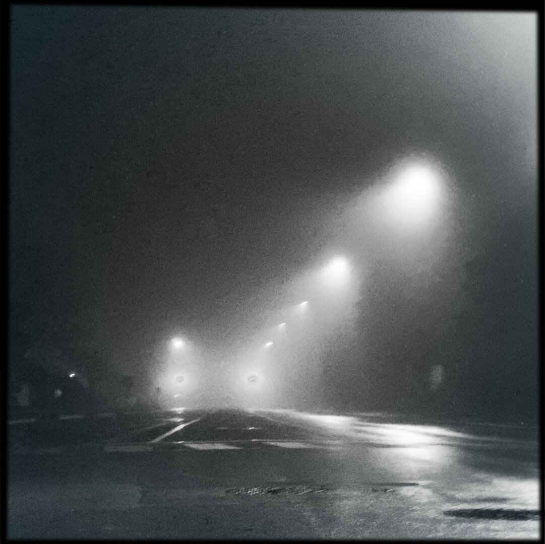 A cold, lonely road in suburbia. Rain and fog, black and white.