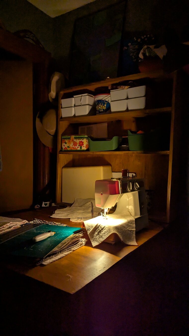 A sewing machine with it's light on in a dark room on a sewing table.