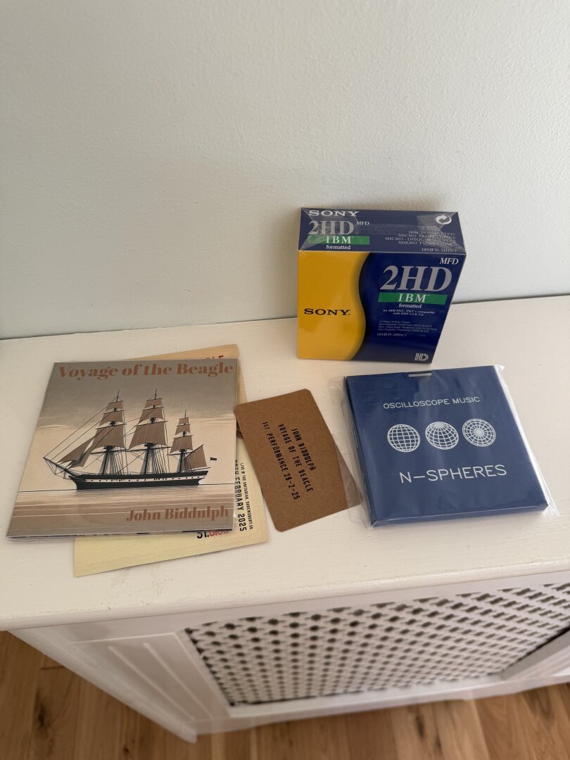 CD, box of 3.5 disks in yellow and blue box, music on 3.5 disk in blue box on white wooden shelf