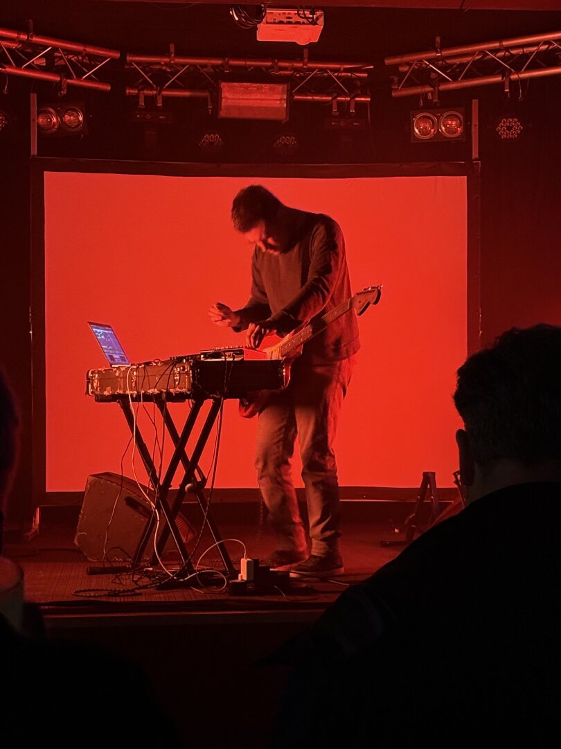 Sulkrooms on stage lit in red with guitar and electronics