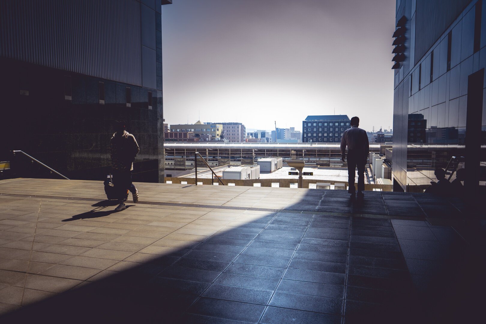 Two people walking at Kyoto Station. One in the sun and one in the shadow.