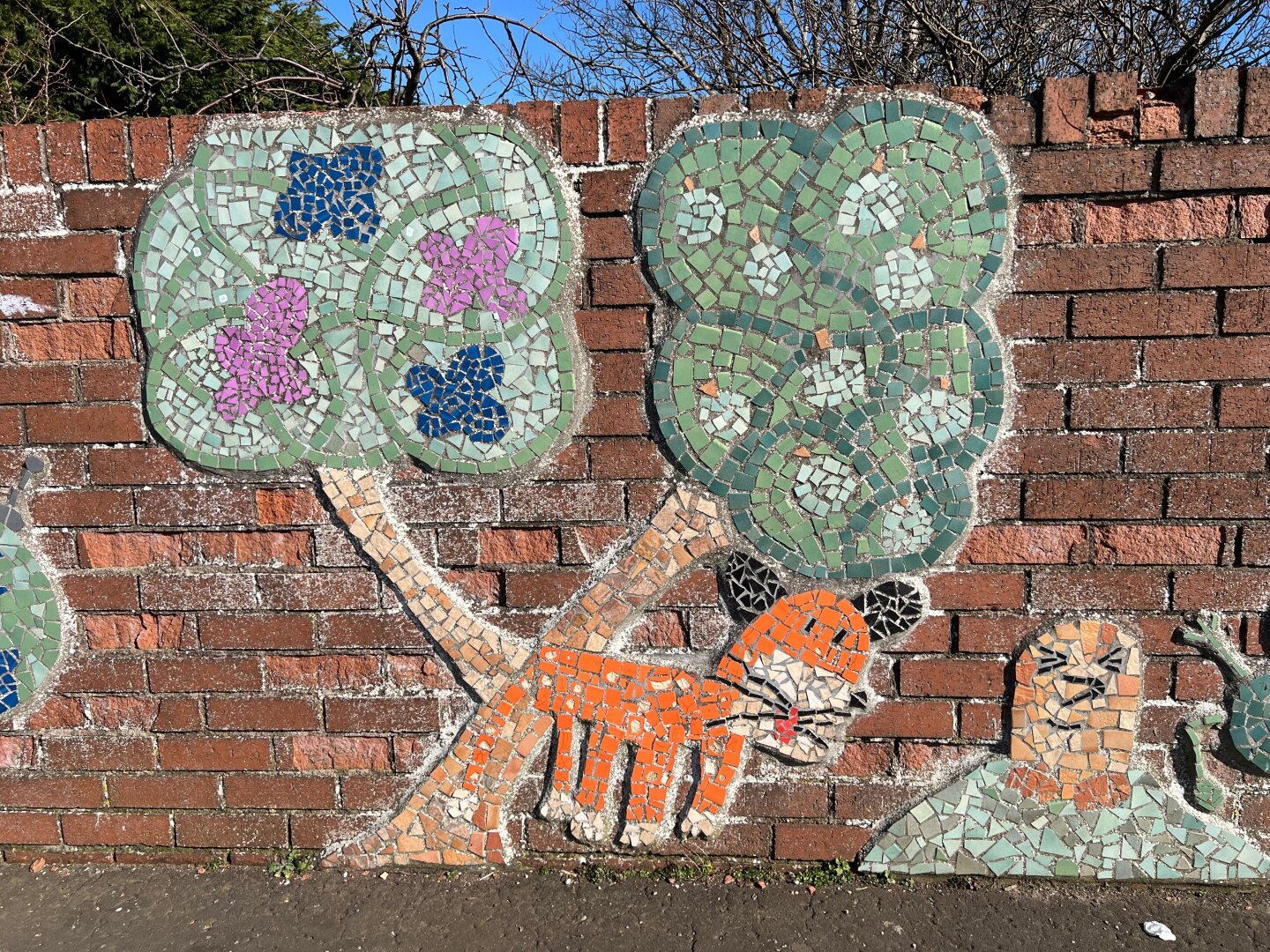 A red brick wall with mosaic trees, fox and mole.