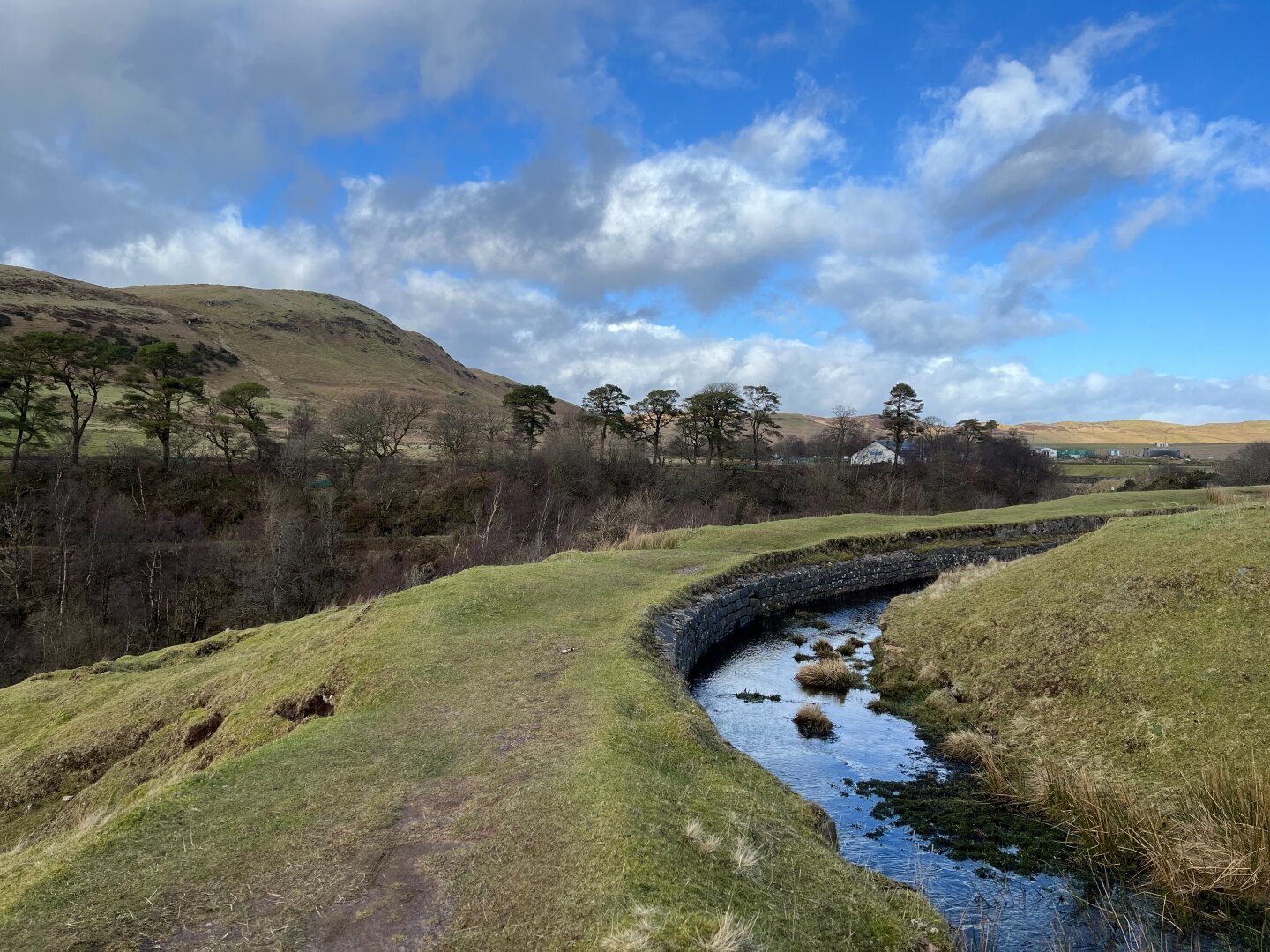Bend of the Greenock Cut with the path next to it and some trees and a hill in the background.