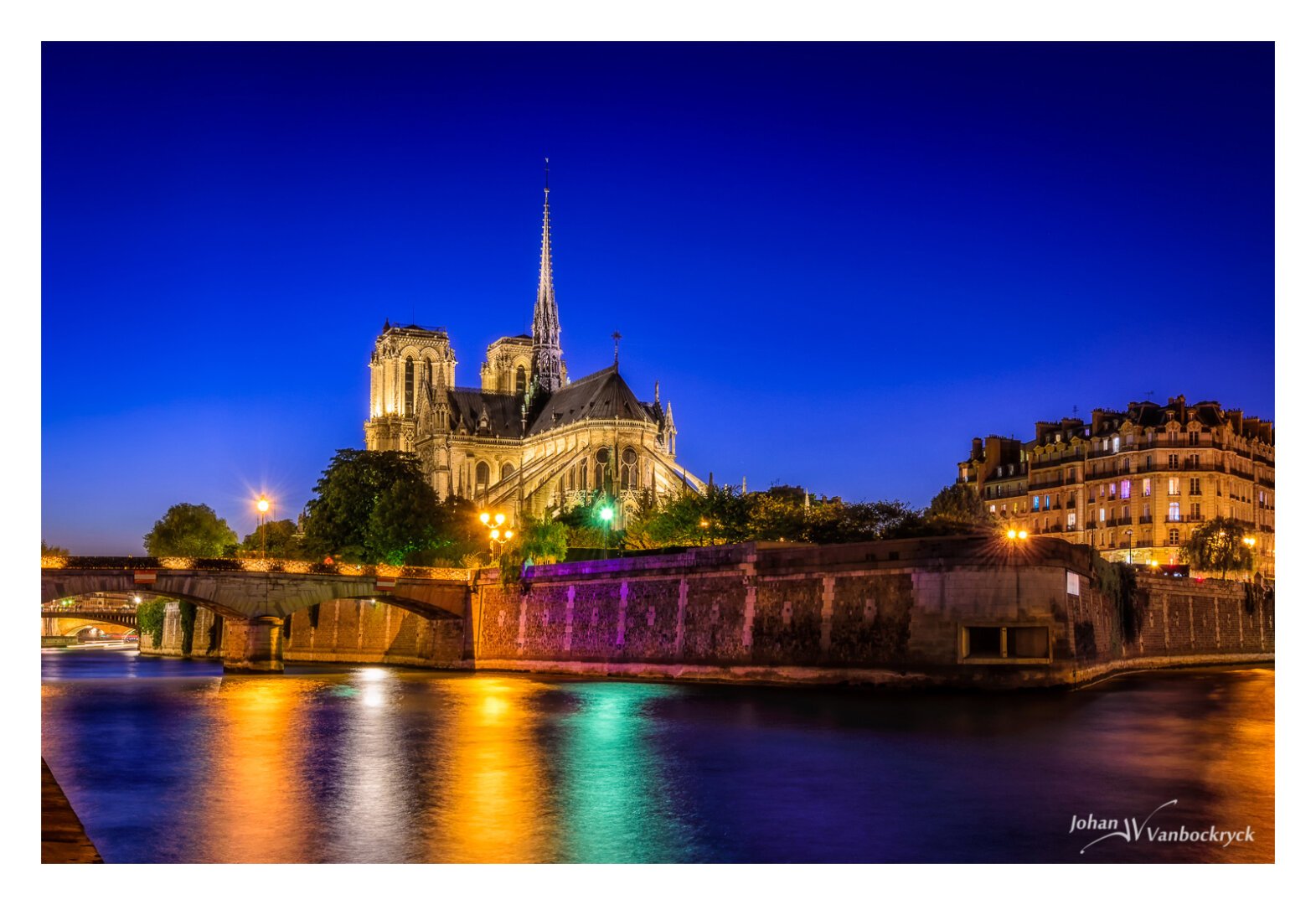 The Notre Dame cathedral at night, with the Seine river in the foreground