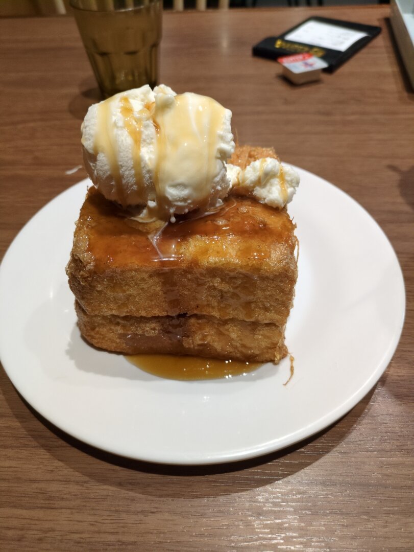 Half a loaf of bread deep fried with a big scoop of vanilla ice cream and maple syrup. Sitting on a white dish on a dark timber table.