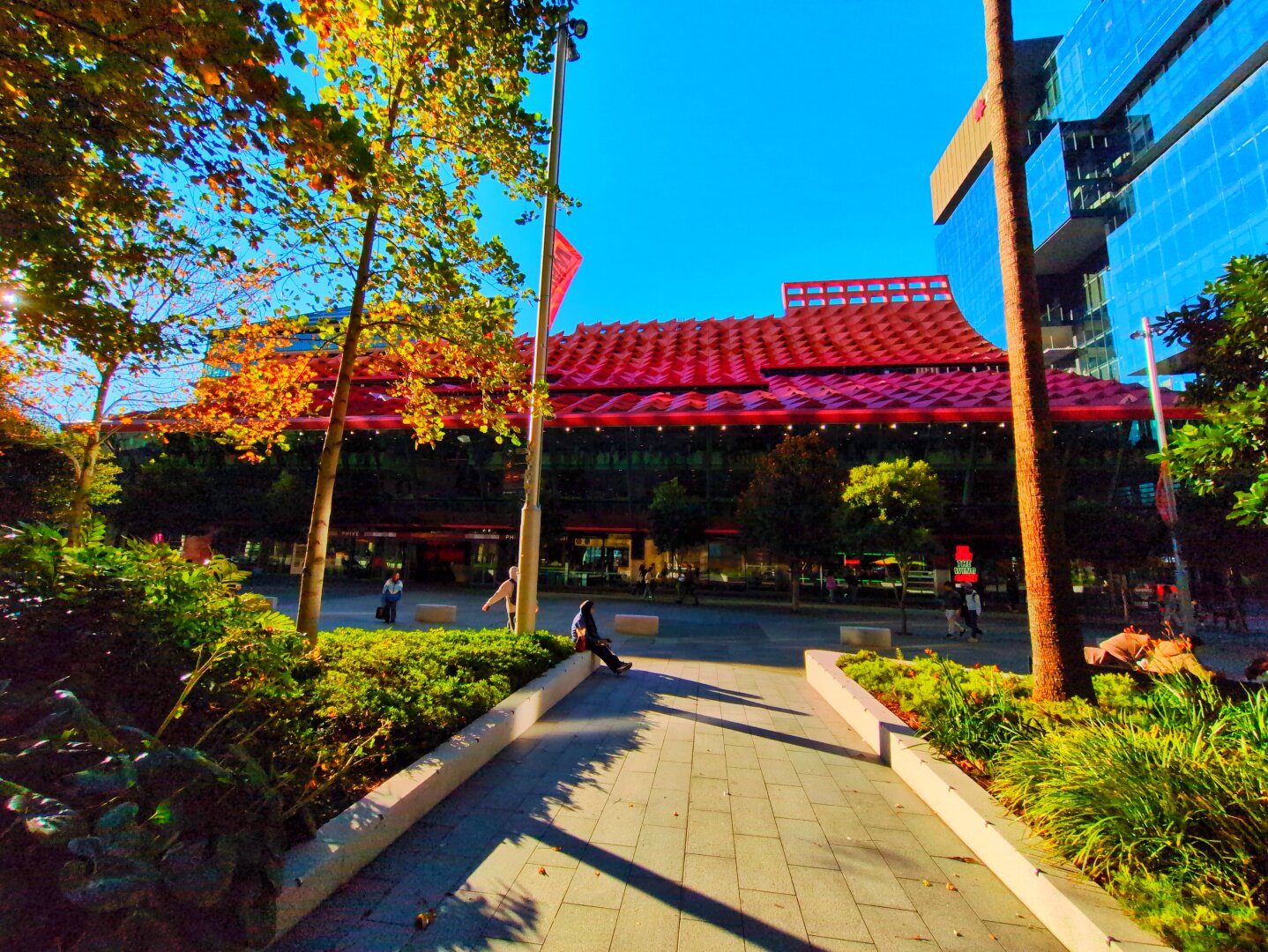 The building as seen directly in front, with plants to the sides and the sloped bright red roof visible.
