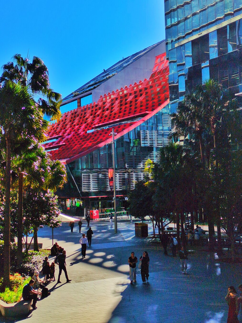 The building framed by trees, as people walk through Parramatta Square.