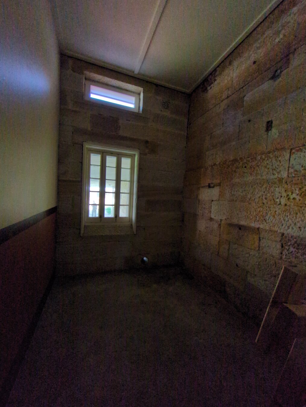 One of the cells. It's very dark, with sandstone on the rear and right wall, and a cream and maroon wall on the left. Two small windows, one above the other, let in some natural light. It's astounding that children as young as 10 used to live here.