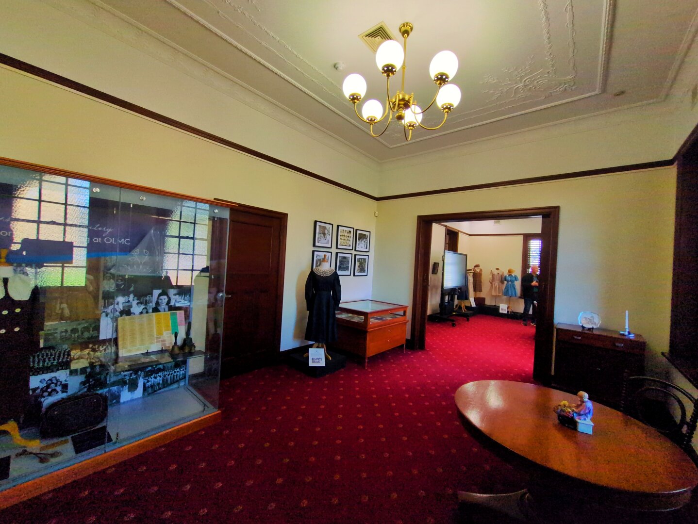 Inside the building. There's dark red carpets, and two-tone cream walls separated by a green railing. The ceiling features intricate plaster cornices and five-light chandeliers.