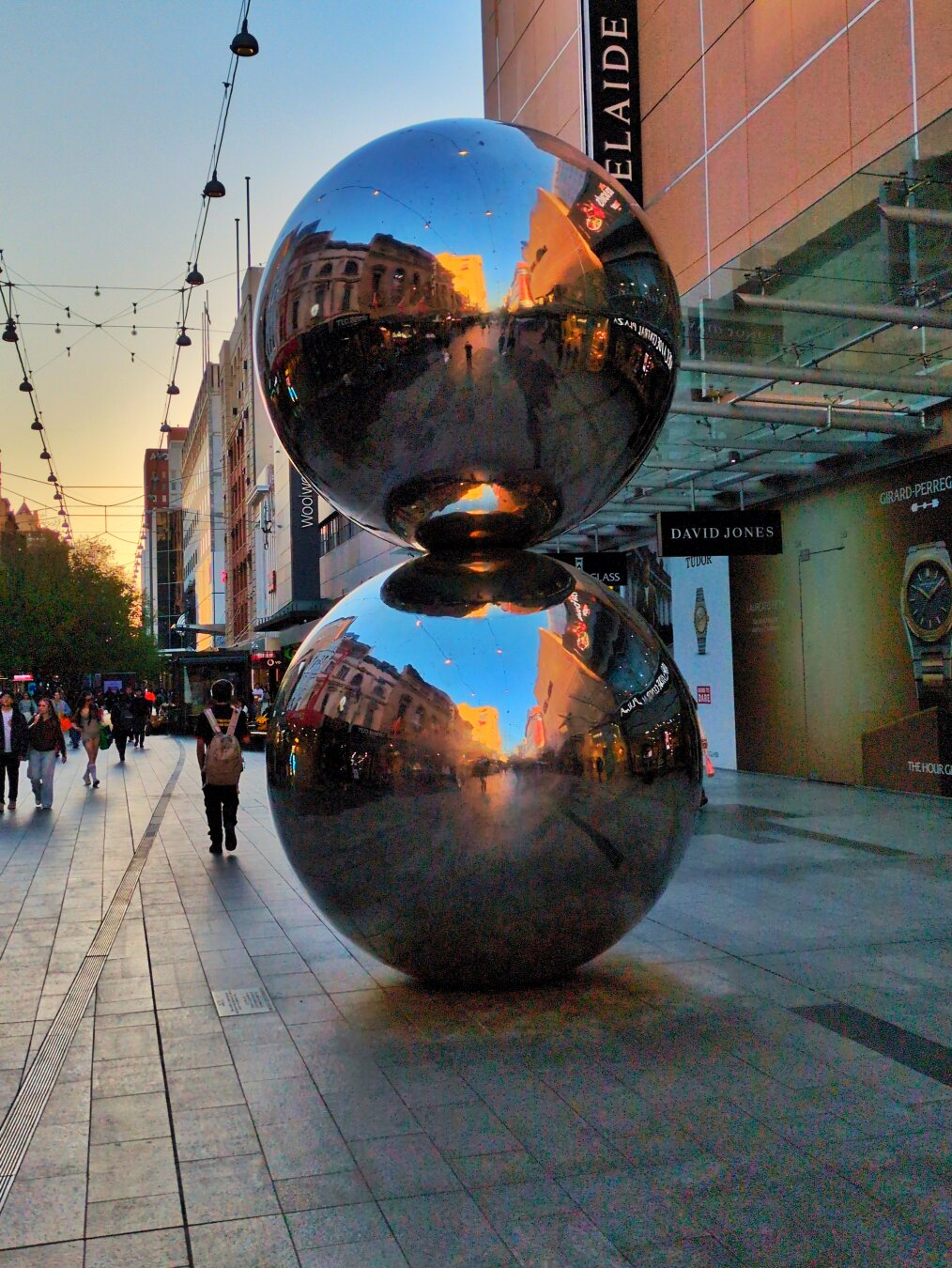 Two large reflective chrome balls stacked on top of each other, standing in a pedestrianised street.