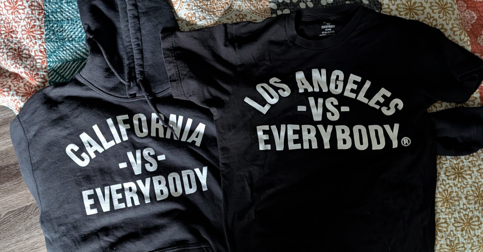 A hoodie that says "California vs. Everybody," next to a t-shirt that says "Los Angeles vs. Everybody."