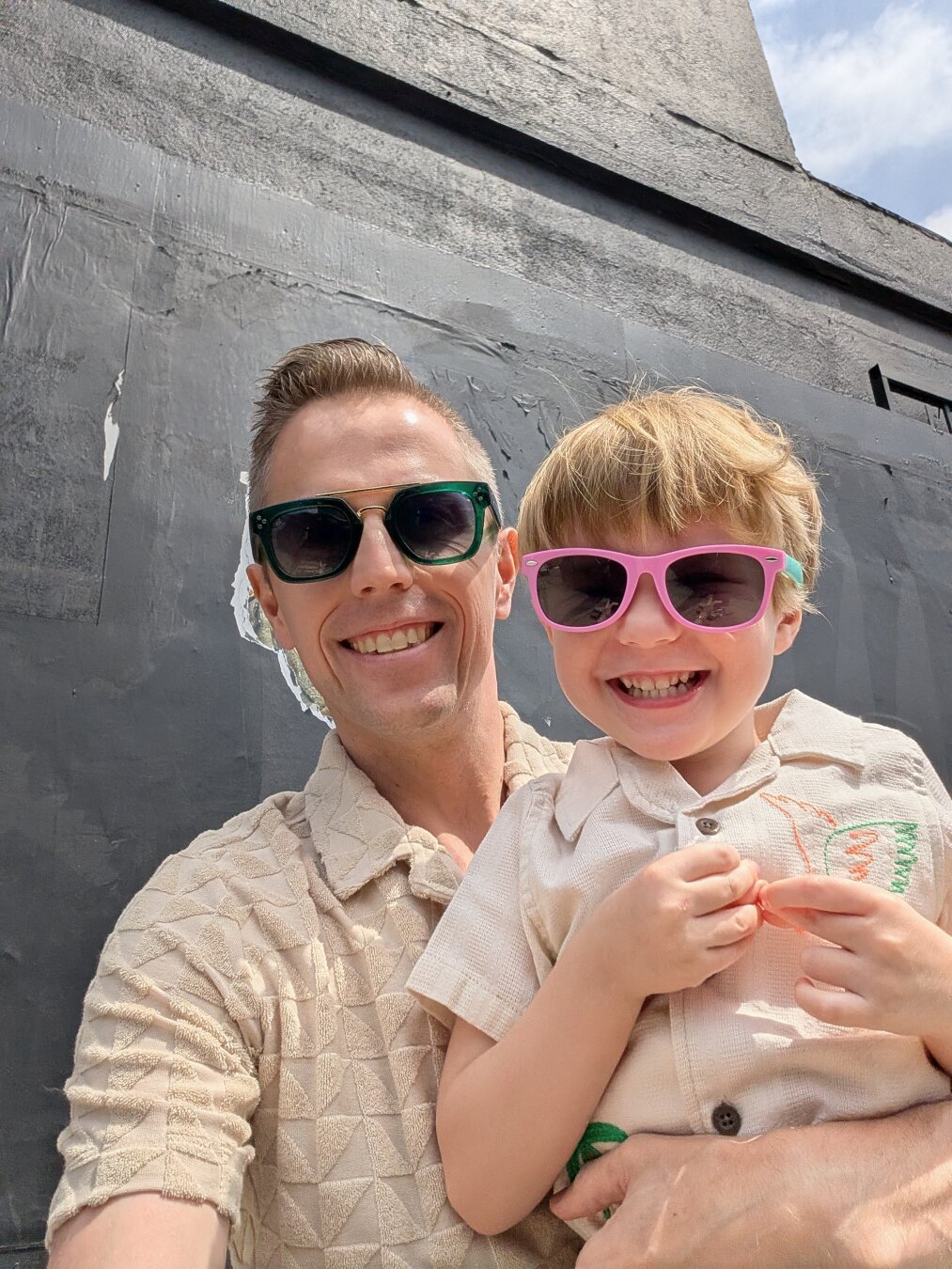 Patrick and his son, PJ, smile, both wearing sunglasses.
