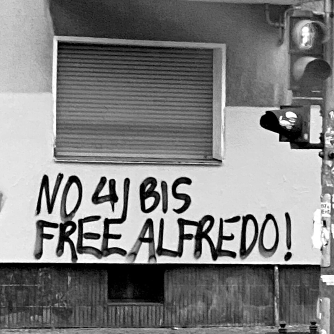 Graffiti over a white wall in a public street that reads: “No 41 Bis Free Alfredo!”